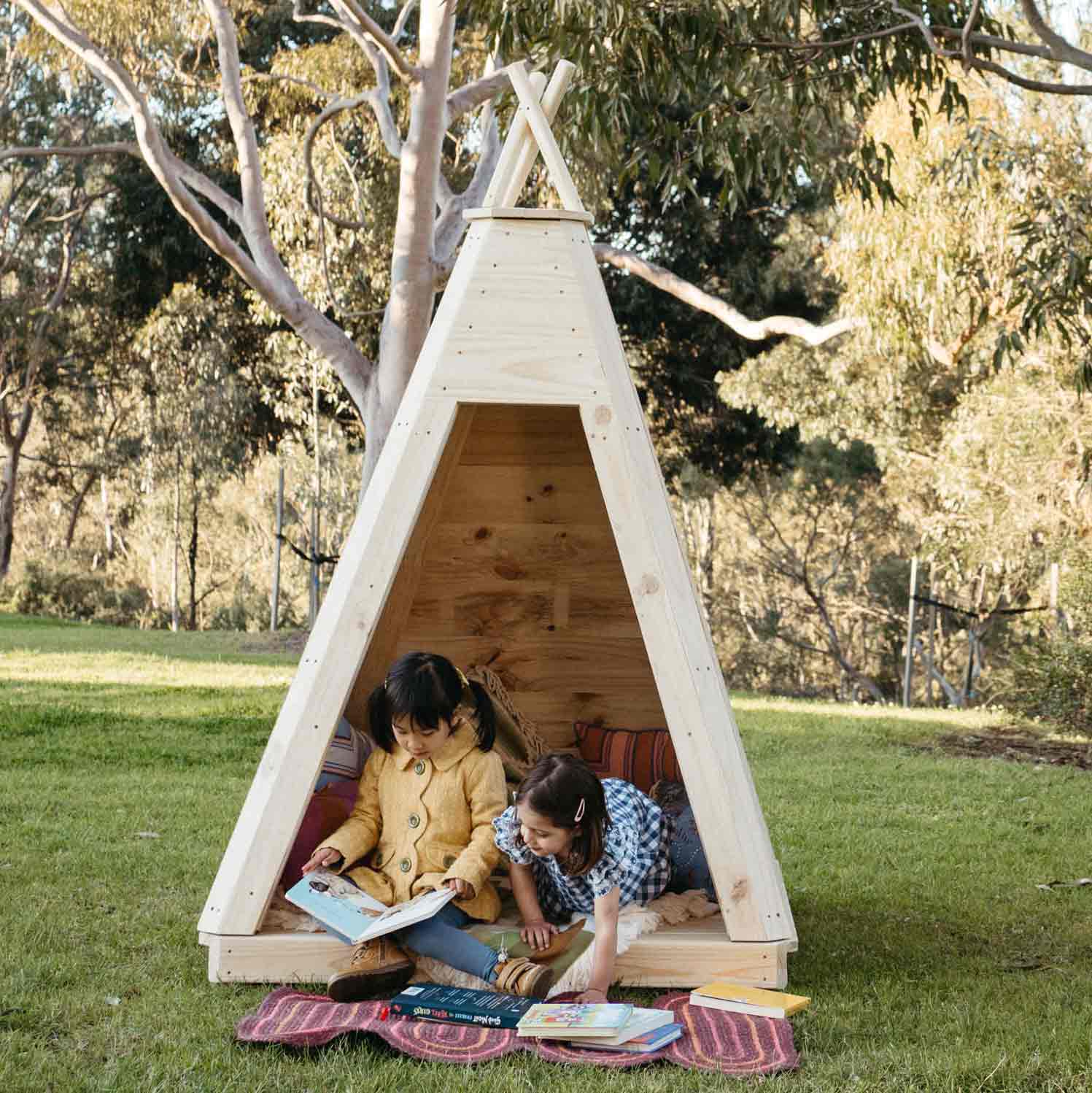 2 young children reading and playing inside a timber Tee Pee built for playground equipment.